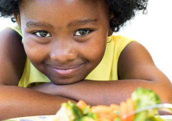 A young girl with a plate of healthy food smiles.