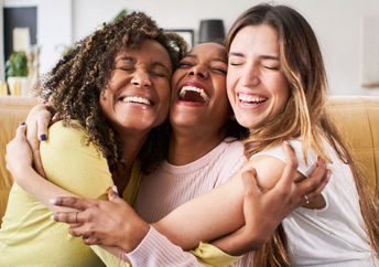 Three smiling friends enjoy a hug.