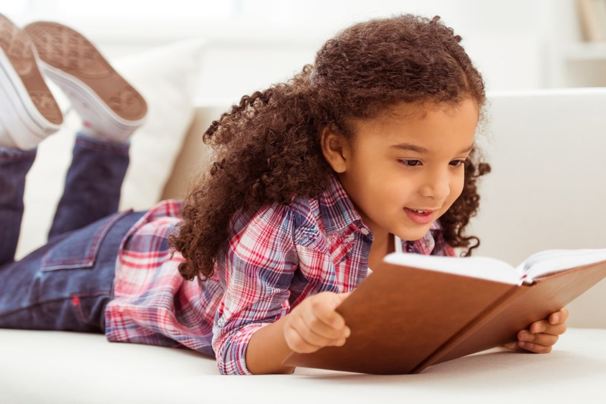 Young girl with curly hair reading a book on the floor Young girl with curly hair reading a book on the floor