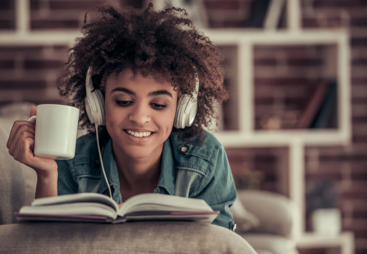 Afro American girl in headphones is listening to music, reading a book, drinking coffee Afro American girl in headphones is listening to music, reading a book, drinking coffee