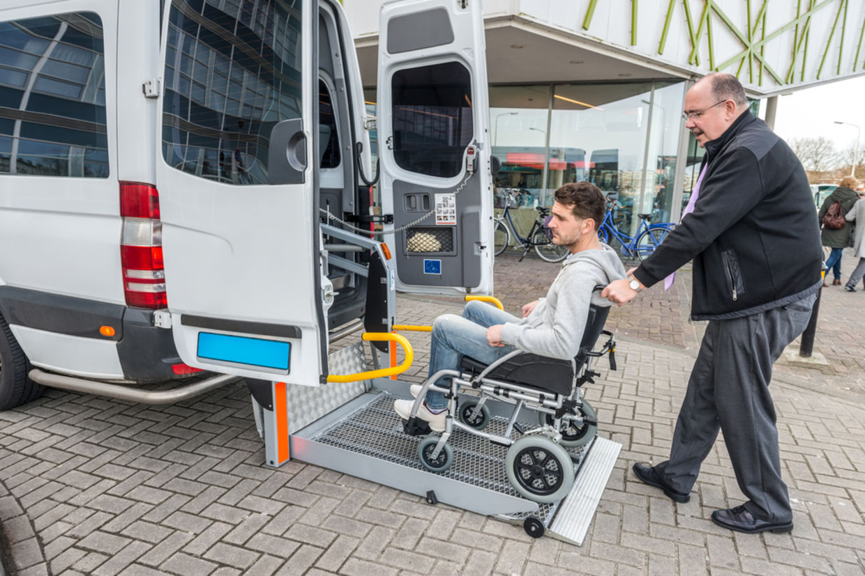 Side view of taxi driver assisting man on wheelchair to board van outside building