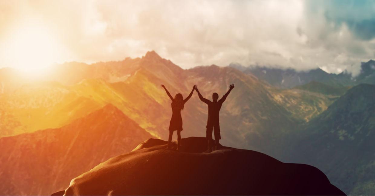 Couple standing on mountain with arms raised Couple standing on mountain with arms raised