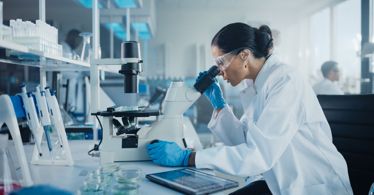 Female scientist in a lab looking under a microscope. Female scientist in a lab looking under a microscope.