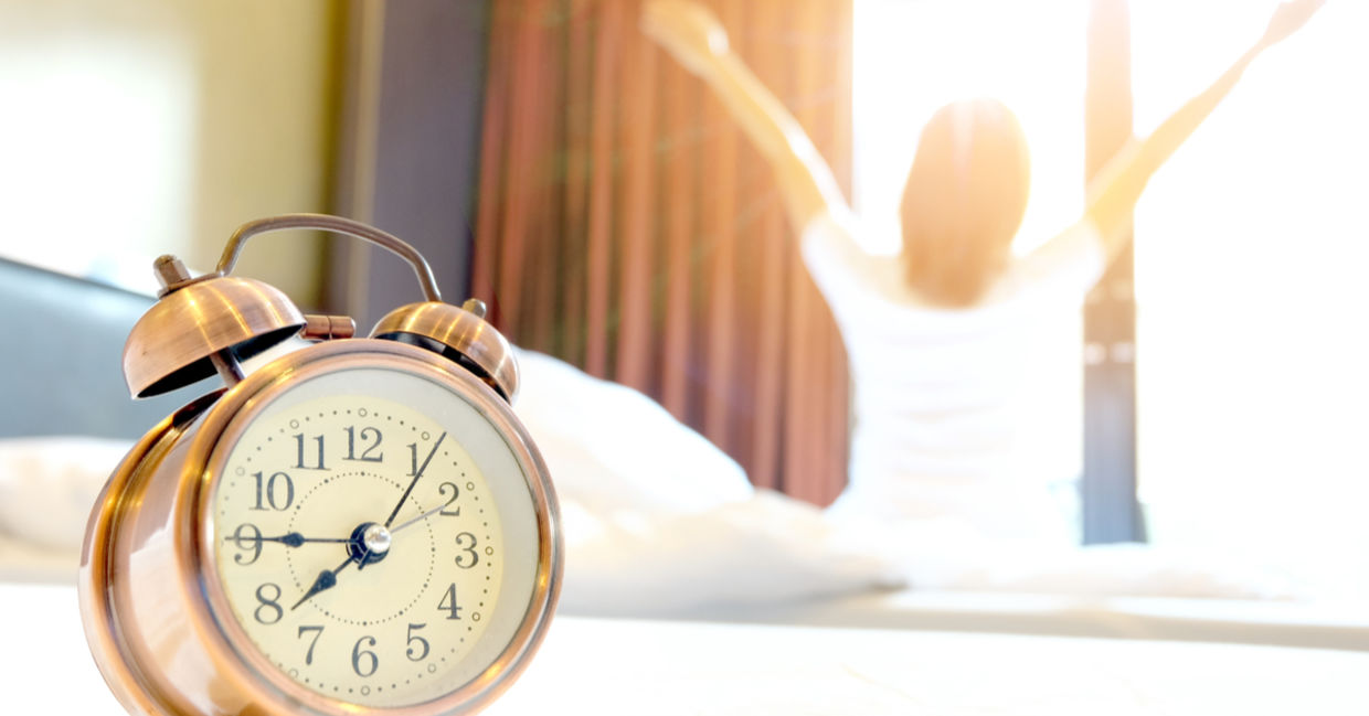 An alarm clock in the bedroom with a woman waking up early looking refreshed. An alarm clock in the bedroom with a woman waking up early looking refreshed.
