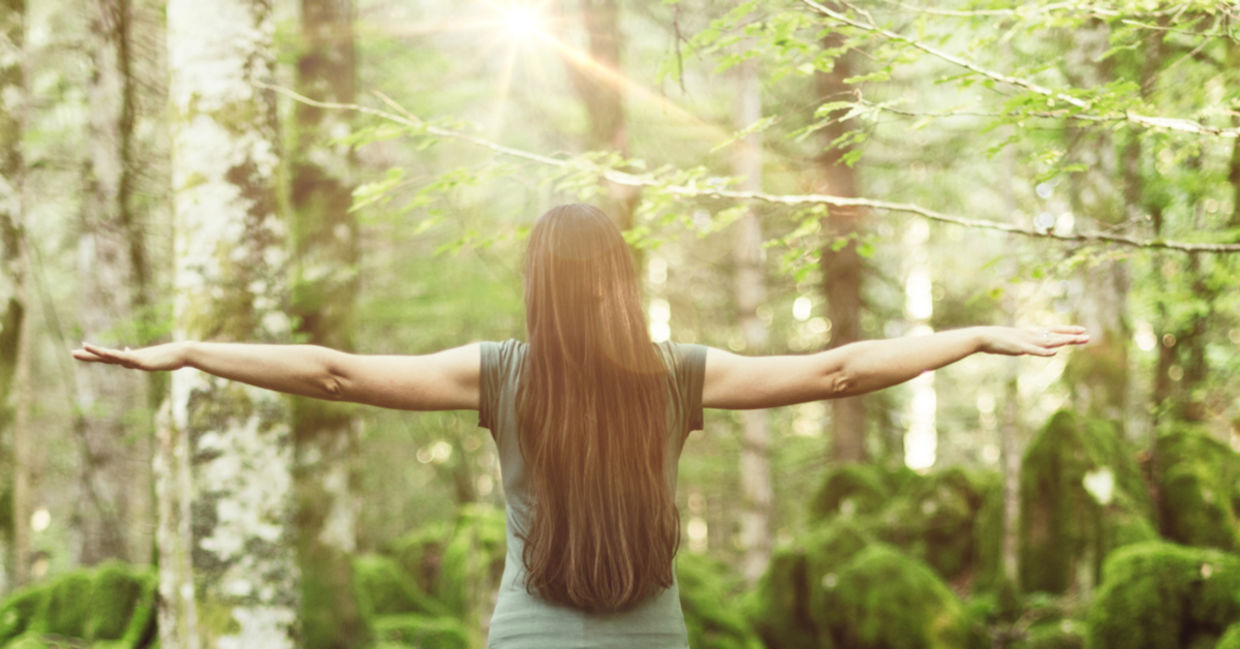 A woman in a forest spreads her arms out wide, showing balance and harmony.