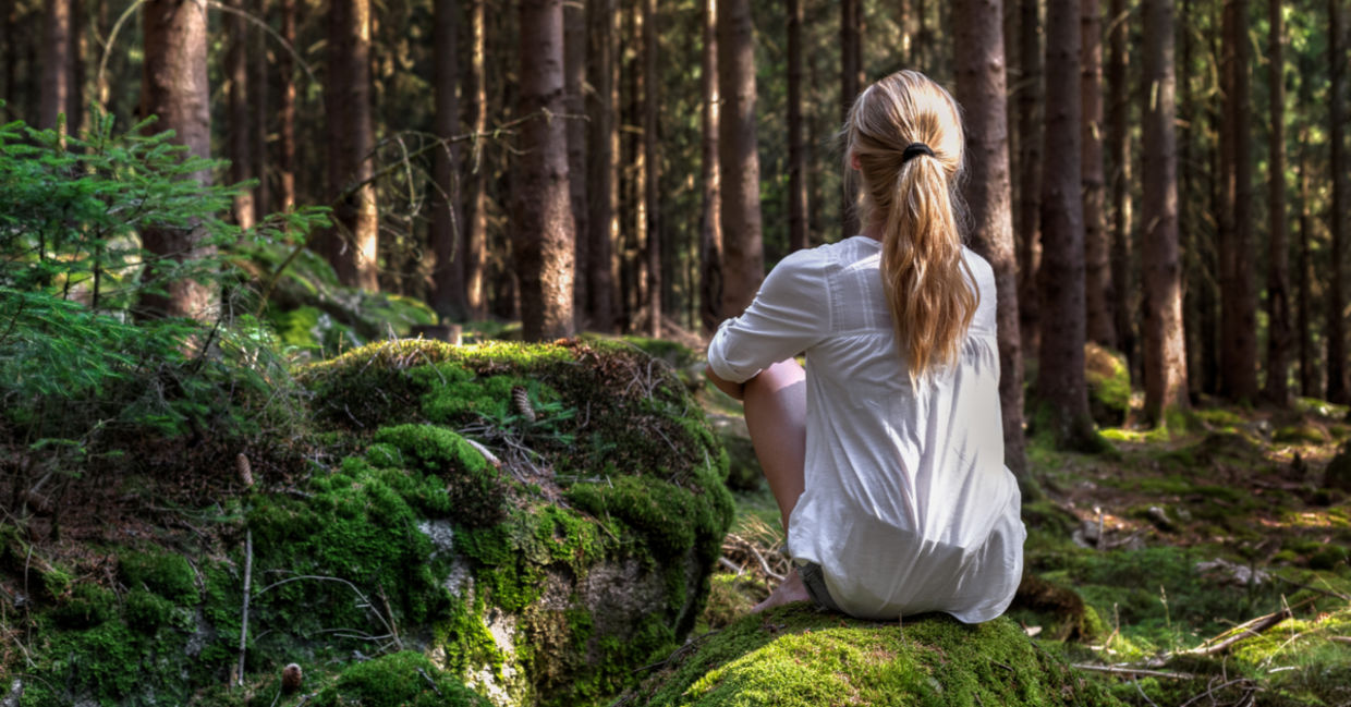 A woman sits on a moss-covered rock enjoying solitude in the forest. A woman sits on a moss-covered rock enjoying solitude in the forest.