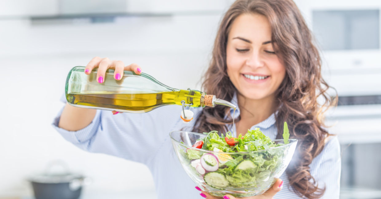 A woman pours olive oil onto a salad. A woman pours olive oil onto a salad.
