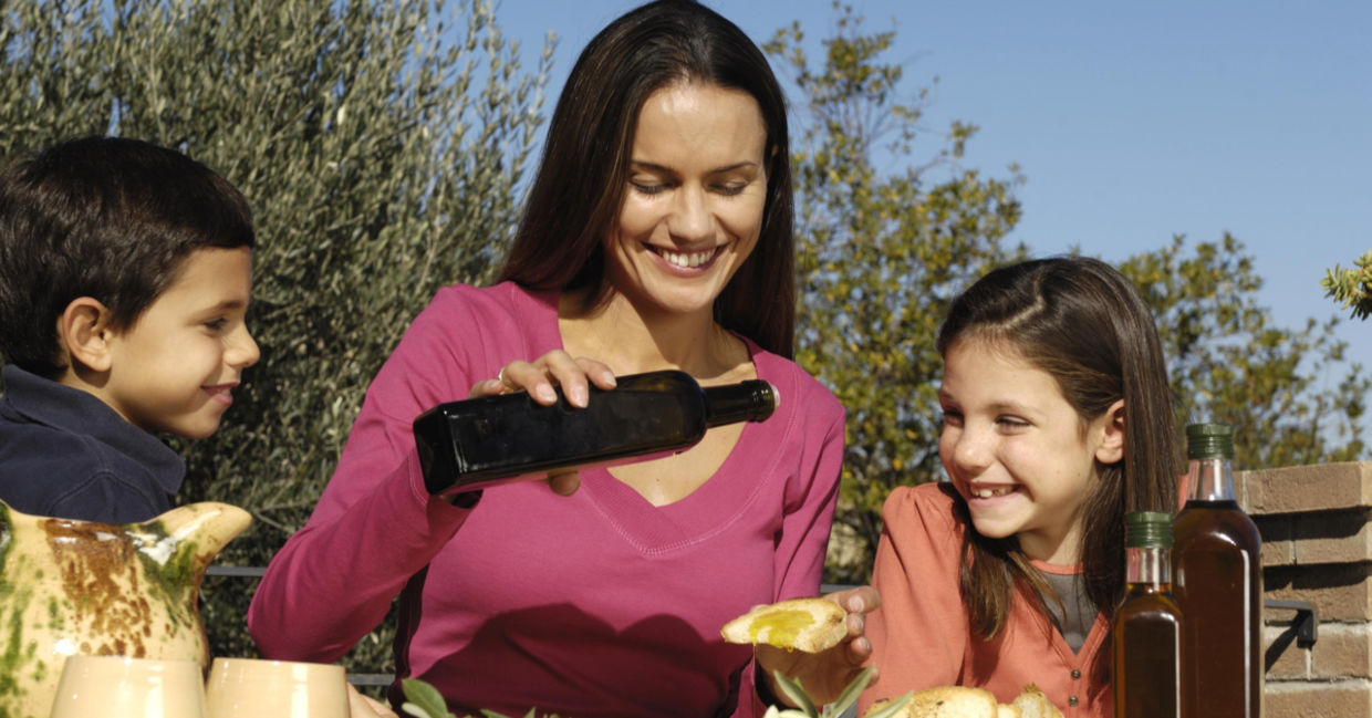 A mother with two young children pours olive oil onto bread. A mother with two young children pours olive oil onto bread.