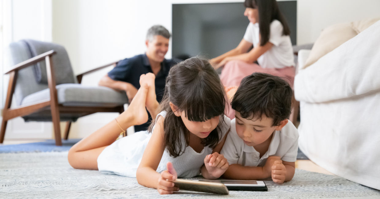 Cute kids lying on floor in living room and using digital gadgets Cute kids lying on floor in living room and using digital gadgets