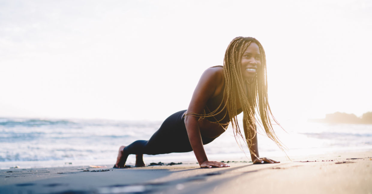 A smiling woman does the plank pose on the sand. A smiling woman does the plank pose on the sand.