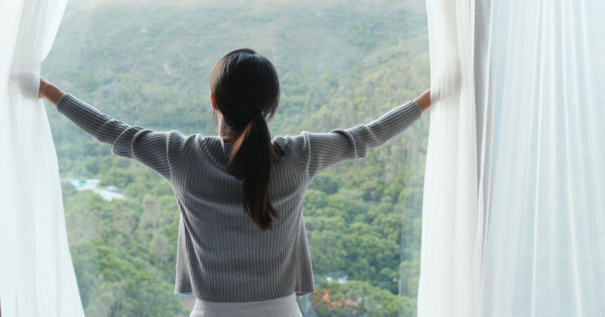 Woman opening a curtain to let in sunlight Woman opening a curtain to let in sunlight