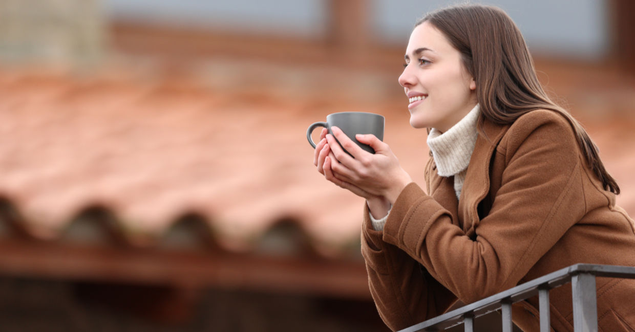 Happy woman contemplating the view and drinking coffee on a balcony in winter Happy woman contemplating the view and drinking coffee on a balcony in winter