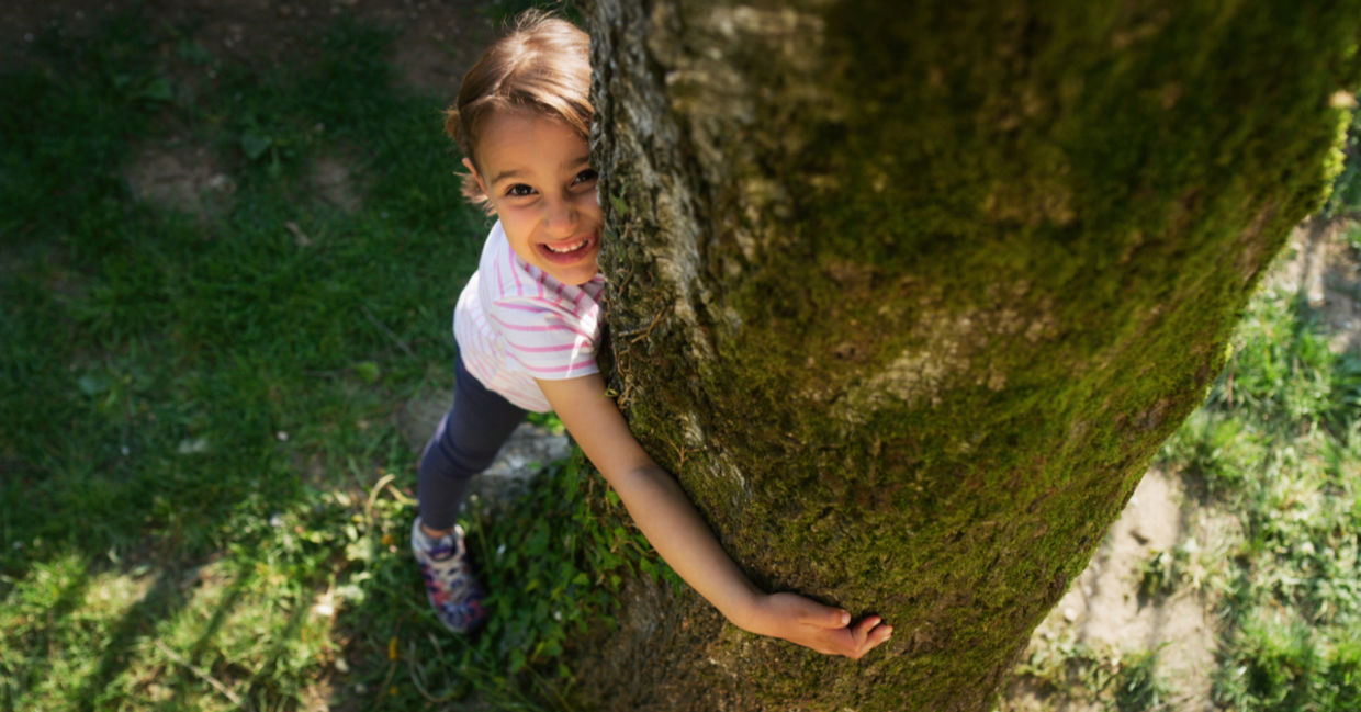 A happy little girl hugging a tree trunk A happy little girl hugging a tree trunk