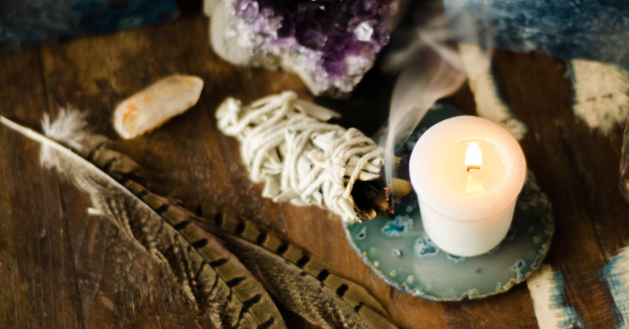 A sage smudge stick, amethyst, a feather, and a lit candle create a sacred space for meditation. A sage smudge stick, amethyst, a feather, and a lit candle create a sacred space for meditation.
