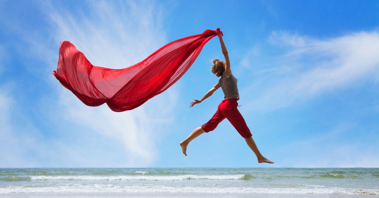 A happy, fulfilled woman jumps on the beach, trailing a bright red scarf high in the air. A happy, fulfilled woman jumps on the beach, trailing a bright red scarf high in the air.