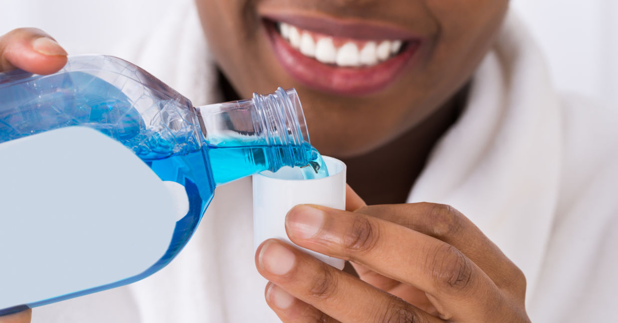 A woman using a DIY tea tree oil mouthwash. A woman using a DIY tea tree oil mouthwash.