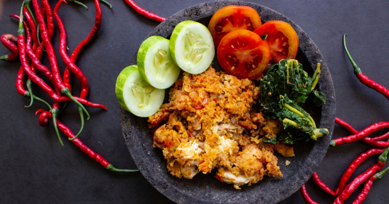 Ayam geprek or chicken crush, Indonesian food made from fried chicken pounded with chili and garlic flavor and served with vegetables and rice. Ayam geprek or chicken crush, Indonesian food made from fried chicken pounded with chili and garlic flavor and served with vegetables and rice.