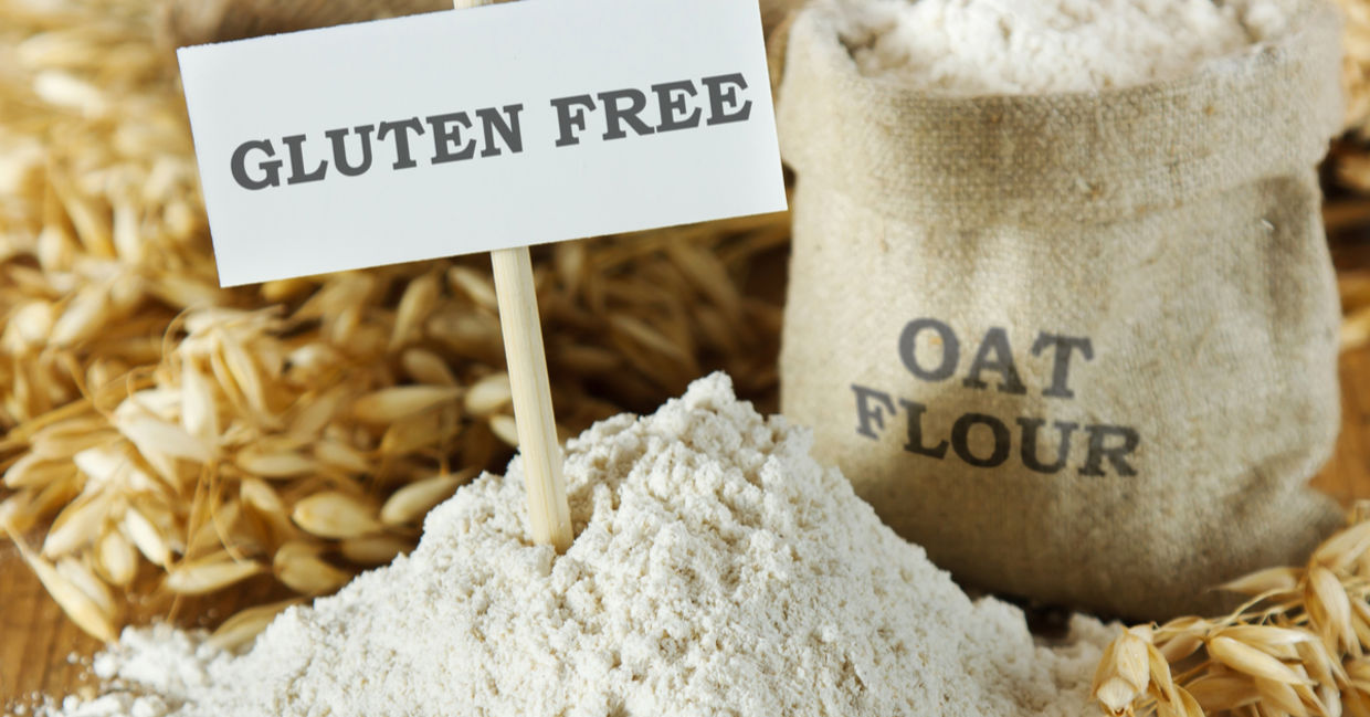 Raw oats, plus a bag of oat flour set beside a sign that reads gluten free. Raw oats, plus a bag of oat flour set beside a sign that reads gluten free.