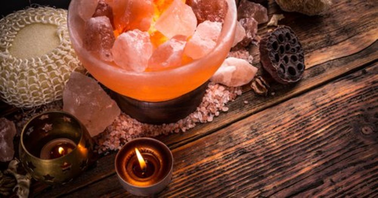 A soothing Himalayan salt lamp, along with tea lights and crystals, are arranged on a wooden surface. A soothing Himalayan salt lamp, along with tea lights and crystals, are arranged on a wooden surface.