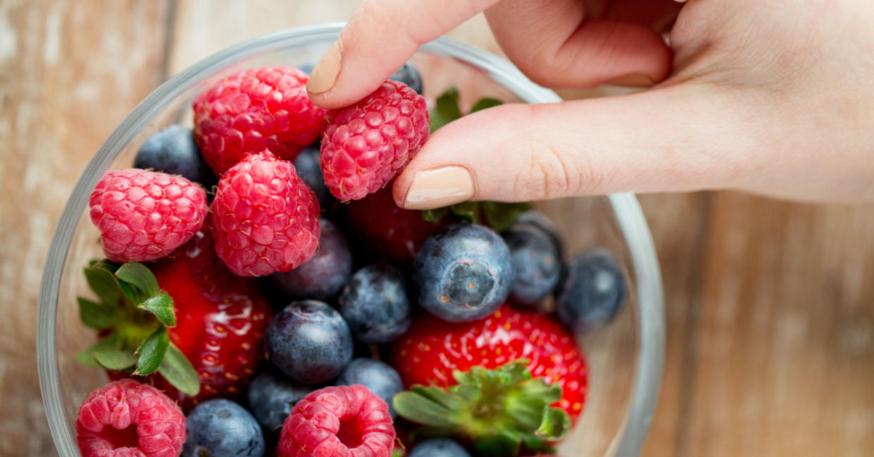 Picking from a bowl of fresh, healthy berries that includes strawberries, raspberries, and blueberries. Picking from a bowl of fresh, healthy berries that includes strawberries, raspberries, and blueberries.
