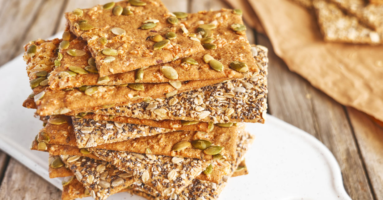 A selection of homemade seed crackers are displayed on a cutting board. A selection of homemade seed crackers are displayed on a cutting board.