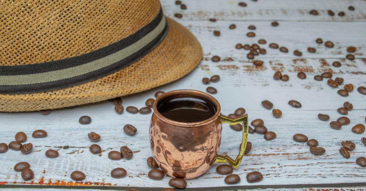 Copper cup with espresso on white wooden table with organic coffee beans with Cuban hat in the background. Copper cup with espresso on white wooden table with organic coffee beans with Cuban hat in the background.