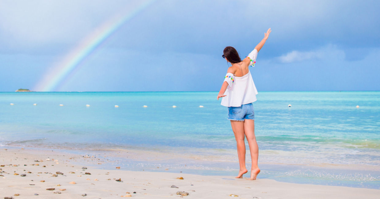 A young woman joyfully walks along a beach with a rainbow on the horizon. A young woman joyfully walks along a beach with a rainbow on the horizon.