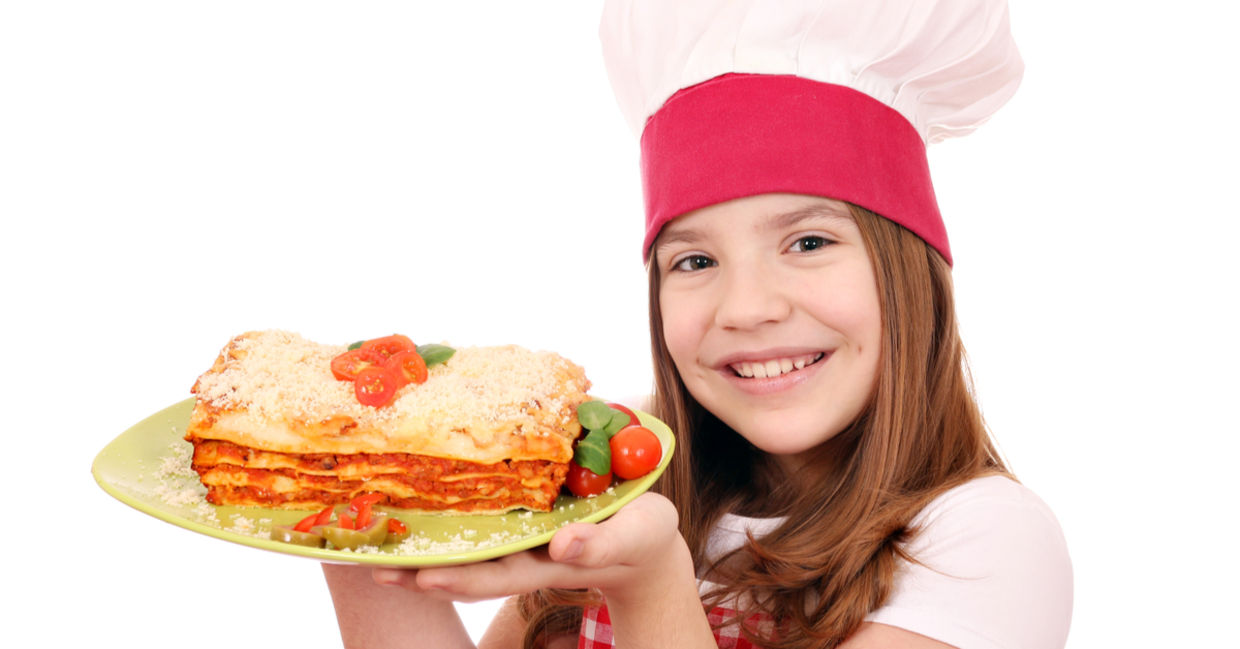 A smiling young girl is holding a plate of lasagna. A smiling young girl is holding a plate of lasagna.