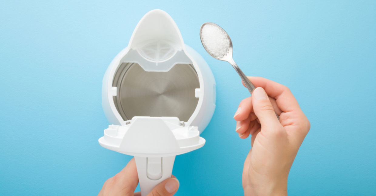 A woman holds a spoon of citric acid to descale a kettle. A woman holds a spoon of citric acid to descale a kettle.