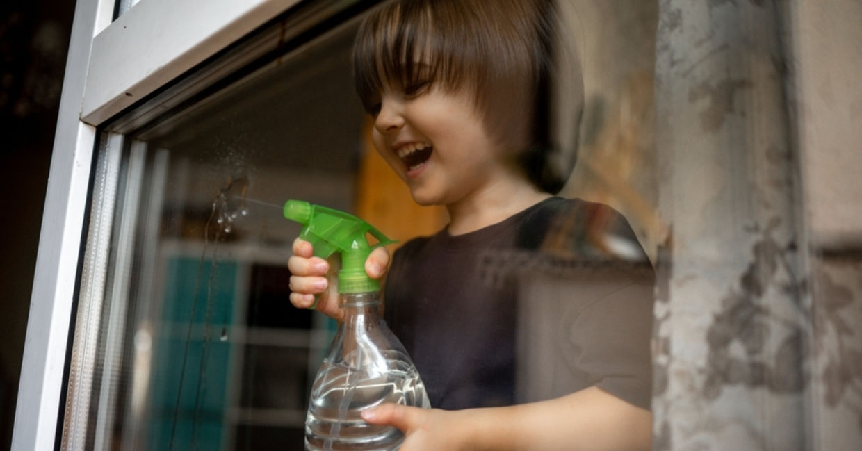 A young boy sprays glass with a DIY organic cleaner. A young boy sprays glass with a DIY organic cleaner.
