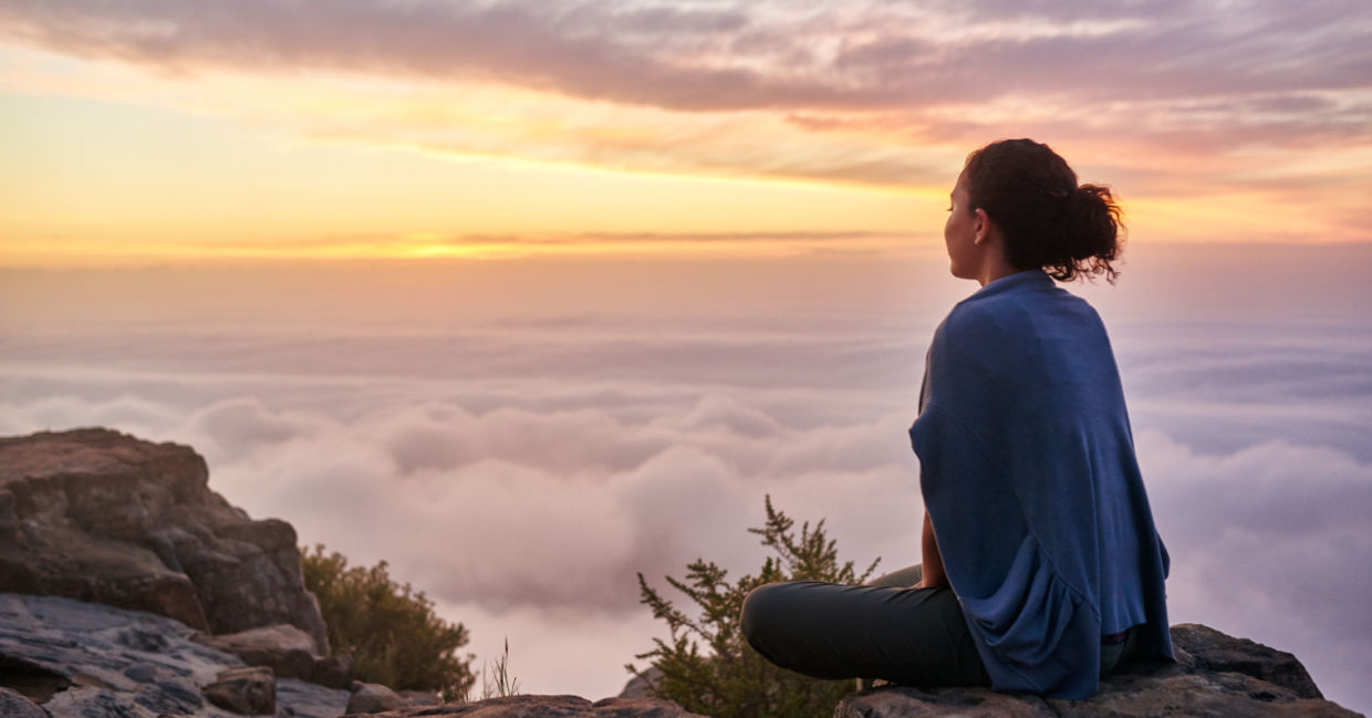 Woman sitting on a mountain top peacefully gazing at clouds Woman sitting on a mountain top peacefully gazing at clouds