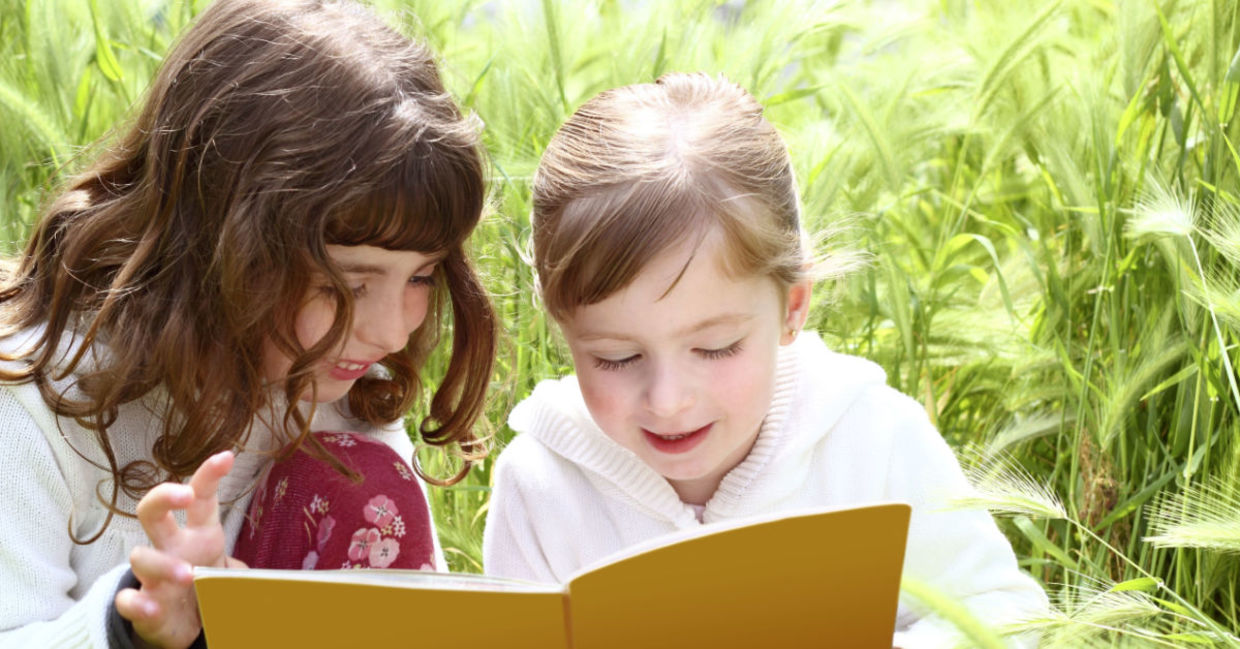 Two girls reading a book they found in a park. Two girls reading a book they found in a park.