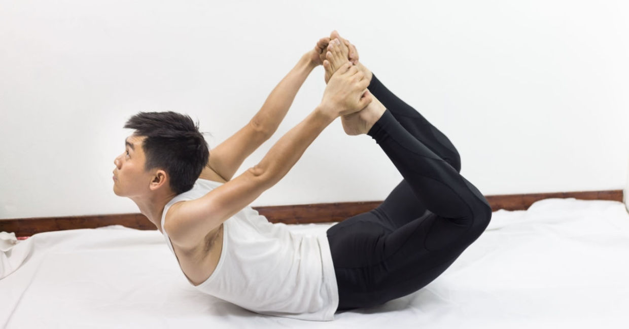 Man doing yoga poses in bed.