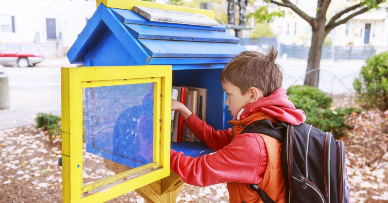 Child taking a book from a little street library. Child taking a book from a little street library.
