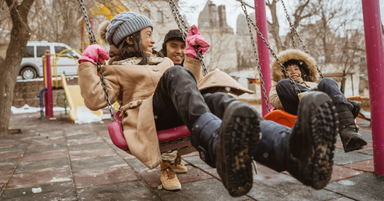 Father swinging his daughter in a playground during the winter. Father swinging his daughter in a playground during the winter.